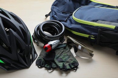 Bicycle cable lock, sunglasses, helmet and fingerless gloves near backpack on wooden table