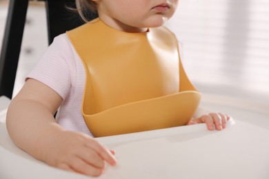Cute little baby wearing bib in highchair at home, closeup
