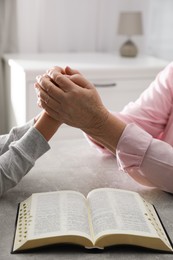 Boy and his godparent praying together at grey table indoors, closeup