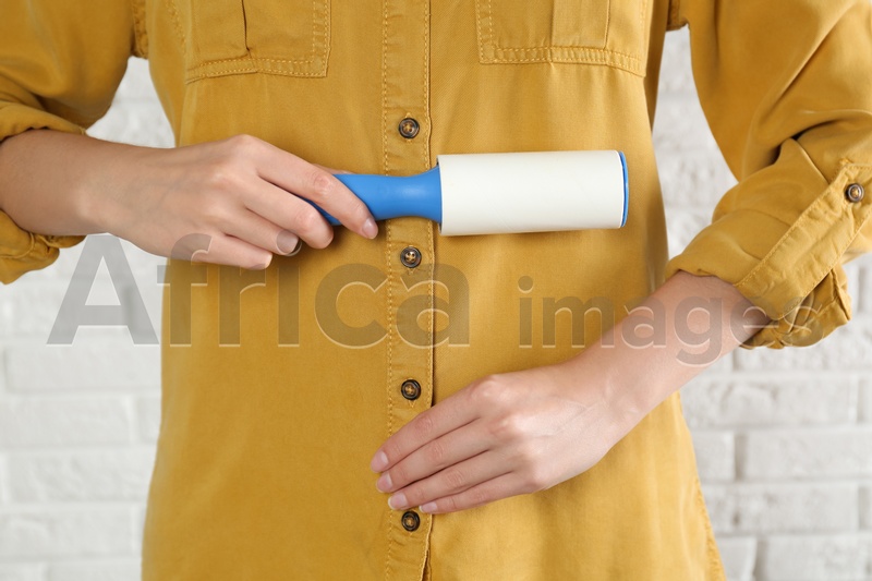Photo of Woman cleaning yellow shirt with lint roller against white brick wall, closeup