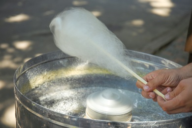 Photo of Man making cotton candy using modern machine outdoors, closeup