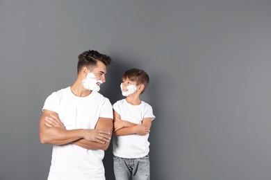 Father and son with shaving foam on faces against color background. Space for text