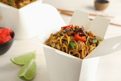 Box of wok noodles with vegetables and meat on white table, closeup