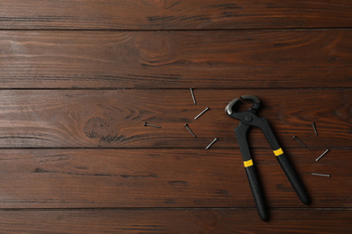 Pincers and nails on wooden background, flat lay with space for text. Carpenter's tool