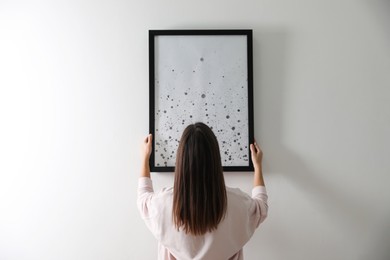 Woman hanging picture on white wall indoors