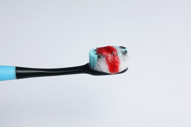 Toothbrush with paste and blood on white background, closeup. Gum inflammation