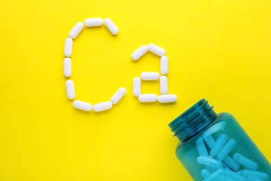 Open bottle and calcium symbol made of white pills on yellow background, flat lay