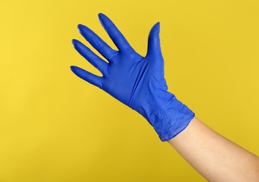 Woman in blue latex gloves on yellow background, closeup of hand