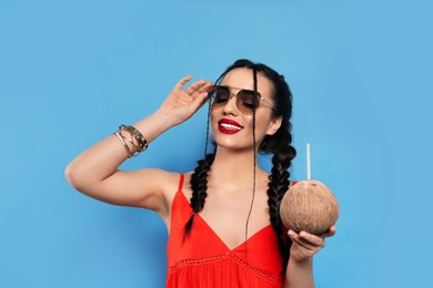 Photo of Young woman with fresh coconut on light blue background. Exotic fruit