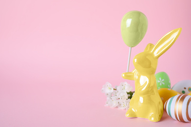 Easter bunny figure, flowers and decorated eggs on pink background. Space for text