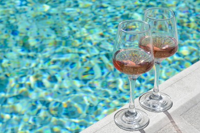 Photo of Glasses of tasty rose wine on swimming pool edge, space for text