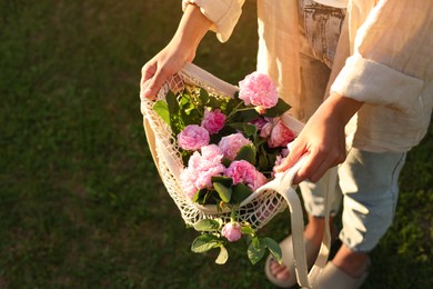 Photo of Woman holding mesh bag with beautiful tea roses outdoors, above view. Space for text