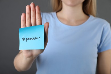 Woman showing sticky note with word Depression on grey background, closeup. Space for text
