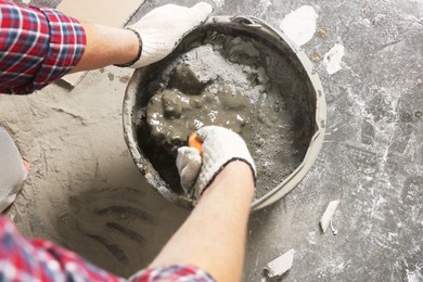 Photo of Worker with trowel mixing cement in bucket indoors, closeup