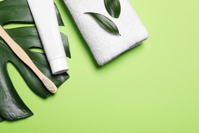 Toothpaste, brush, leaves and towel on light green background, flat lay. Space for text