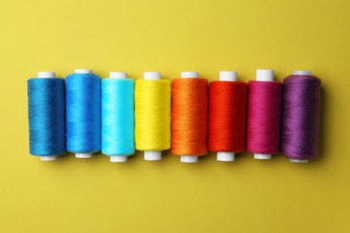 Photo of Set of different colorful sewing threads on yellow background, flat lay