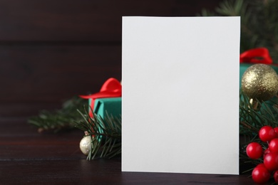 Blank greeting card near Christmas decorations on wooden table, closeup. Space for text