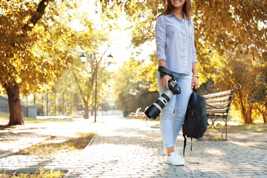 Young female photographer with professional camera and backpack in park. Space for text