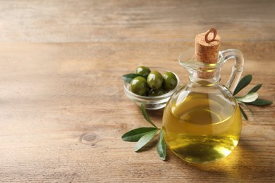 Glass jug of oil, ripe olives and green leaves on wooden table. Space for text