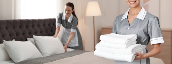 Chambermaid with stack of fresh towels in hotel room, closeup view with space for text. Banner design