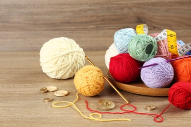 Clews of colorful knitting threads, crochet hooks, measuring tape and buttons on wooden table
