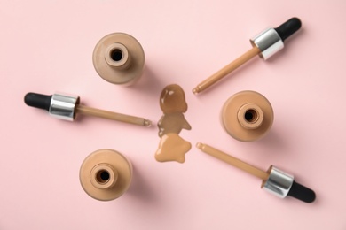 Bottles of liquid foundation and droppers on pink background, flat lay