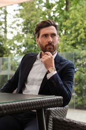 Photo of Pensive bearded man looking away in cafe outdoors