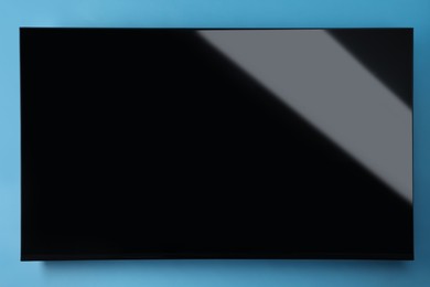 Photo of Modern TV with blank wide screen on light blue background