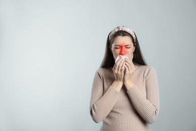 Young woman with tissue suffering from runny nose on light background. Space for text