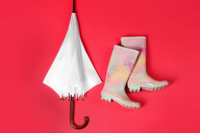 Beautiful white umbrella and colorful rubber boots on red background, flat lay