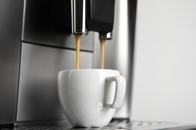 Espresso machine pouring coffee into cup against light background, closeup