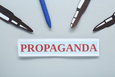 Information warfare concept, journalism and media influence. Pen and paper bullets aimed at card with word Propaganda on white background, flat lay