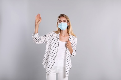 Woman in protective face mask showing hello gesture on grey background. Keeping social distance during coronavirus pandemic