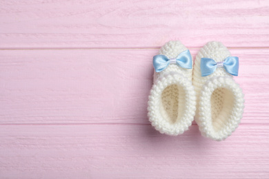 Top view of child's booties on pink wooden background, space for text