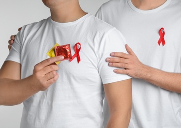 Men with condoms and AIDS awareness ribbon on white background, closeup