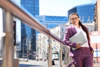 Photo of Beautiful businesswoman with laptop in city on sunny day