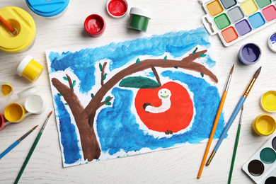 Flat lay composition with child's painting of apple tree with worm on white wooden table