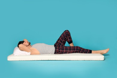 Man in sleeping mask resting on soft mattress against light blue background