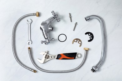 Parts of water tap and wrenches on white marble countertop, flat lay