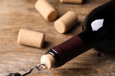 Opening wine bottle with corkscrew on wooden table, closeup