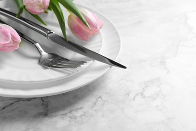 Photo of Stylish table setting with cutlery and tulips on white marble background, closeup. Space for text