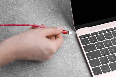 Woman plugging USB cable with type C connector into laptop port at grey table, closeup