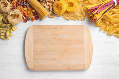 Different types of pasta and cutting board on white wooden table, flat lay. Space for text
