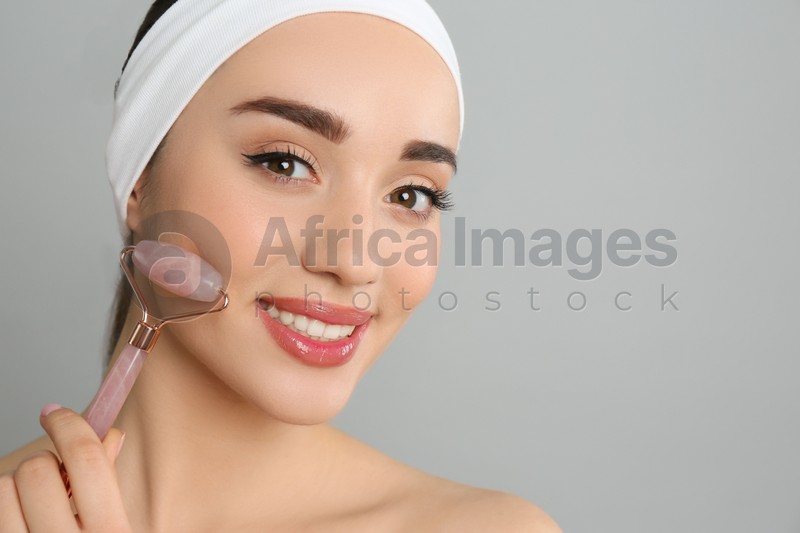 Photo of Woman using natural pink quartz face roller on grey background, closeup. Space for text