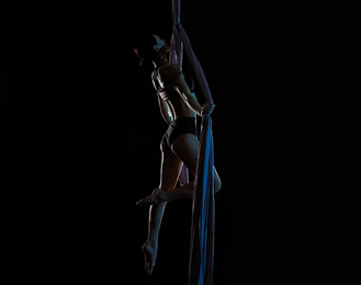 Young woman performing acrobatic element on aerial silk indoors