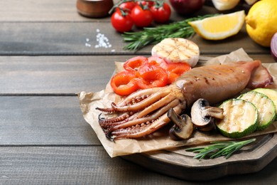 Tasty grilled squid with vegetables served on wooden table, space for text