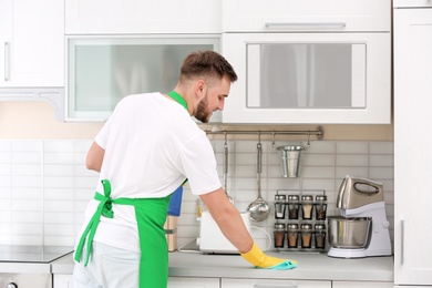 Young man in uniform cleaning kitchen counter