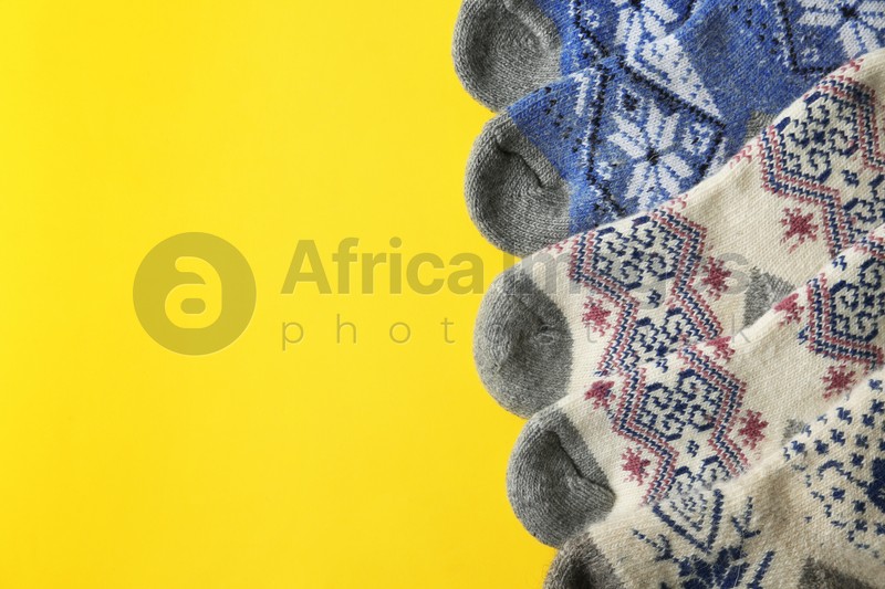Soft knitted socks on yellow background, flat lay with space for text. Winter clothes