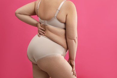 Overweight woman in beige underwear on pink background, closeup. Plus-size model