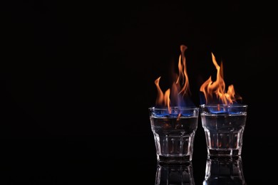 Flaming vodka in shot glasses on black background, space for text